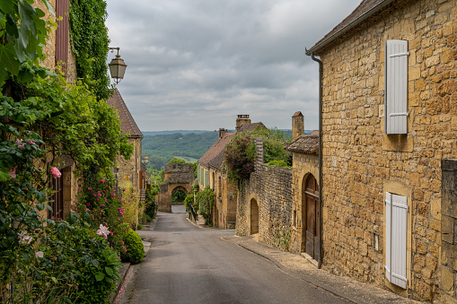 Domme, France - 12 May, 2022: picturesque street with stone houses and blossoming flowers in the historic village of Domme in the Dordogne Valley