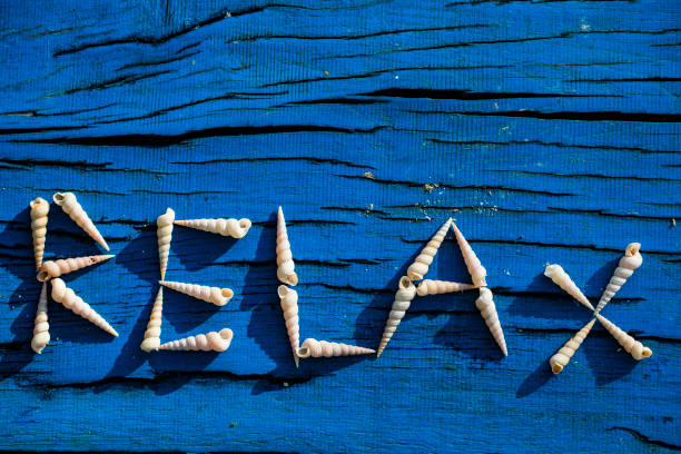 Word Relax Written With Arranged Seashells on Blue Wood From Directly Above.