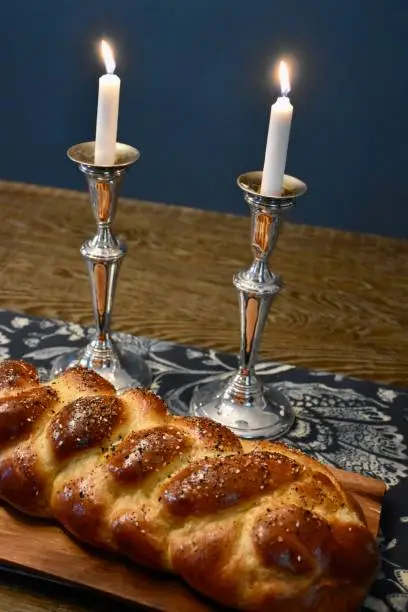 Two lit shabbat candles in silver candlesticks on table with freshly baked challah