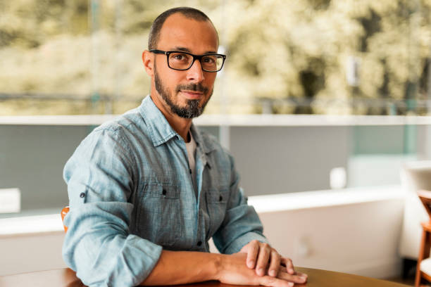 istock Bearded man wearing eyeglasses sitting on a chair by a table looking at camera 1398466631