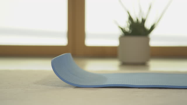CLOSEUP Unrolling blue yoga mat across the floor for home workout in living room