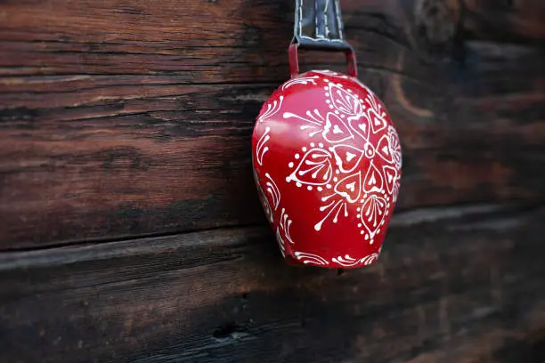 Traditional swiss cow bell red and white, decorative souvenir, on wooden background