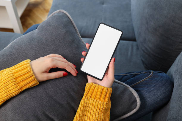 Young woman hand holding smart phone with mockup white blank display, empty screen for social media app ads at home.