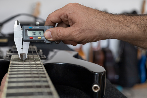 Latin American luthier calibrates the strings of an electric guitar with a digital vernier. Unrecognizable. Guitar concept, calibration, instrument.