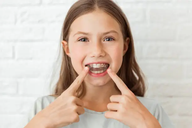 Attractive little girl shows index fingers myofunctional trainer. Help equalize the growing teeth and correct bite, develop mouth breathing habit. Corrects the position of the tongue