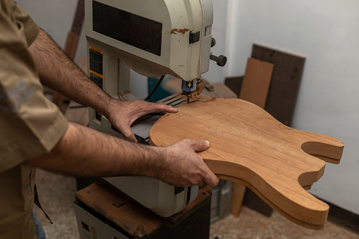 Close-up of unrecognizable Latin American luthier making an electric guitar with a saw. Stringed instrument construction concept