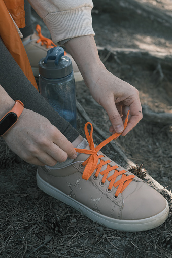 Feet in sneakers on forest ground. Female hands are tying shoelace