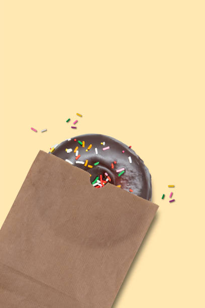 istock Classic freshly baked Chocolate donut with colorful sprinkles inside paper bag package isolated on white background 1398486604