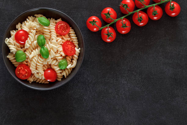 istock Fusilli, cooked pasta with tomatoes cherry and basil, on dark background, top view, space to copy text. 1398490270