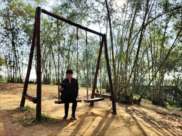 An Asian woman is using laptop and digital tablet working while sitting on bamboo swing at sub-urban town.