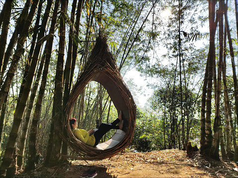 An Asian woman is using laptop working while lying down in bamboo nest at sub-urban town.