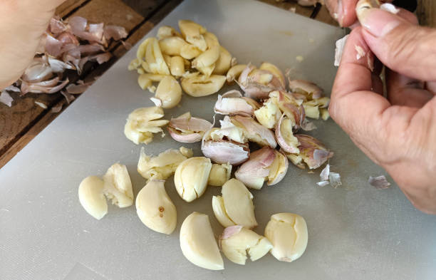 Woman peeling garlic on the cutting board for cooking Woman peeling garlic on the cutting board for cooking. garlic bulb photos stock pictures, royalty-free photos & images
