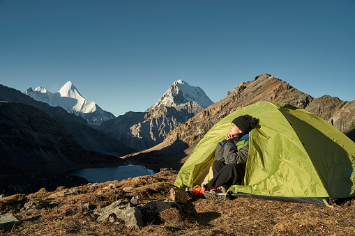 asian woman female camper sitting in tent enjoying the early morning sunlight with eyes closed in yading national park, daocheng county, sichuan province, china