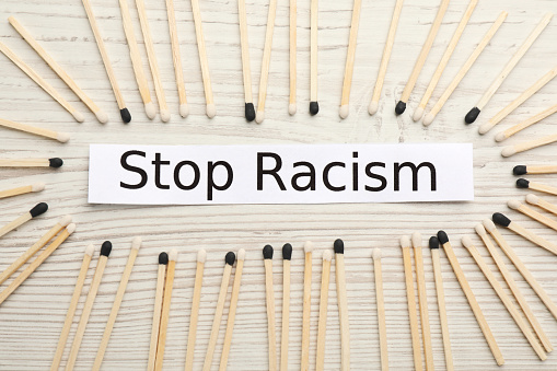 Phrase Stop Racism and different matches on white wooden table, flat lay