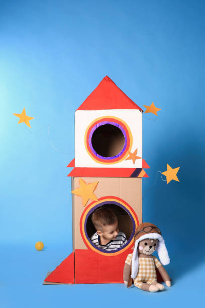 istock Cute little boy playing with cardboard rocket on light blue background 1398514540