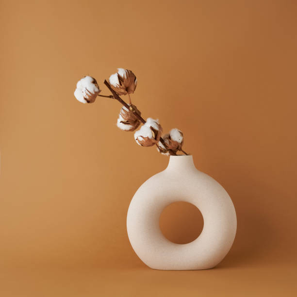 Round ceramic vase with a cotton branch on a brown background. Copy space