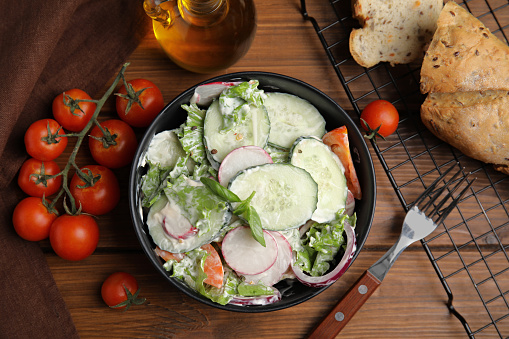 Bowl of delicious vegetable salad dressed with mayonnaise and ingredients on wooden table, flat lay