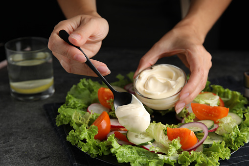 Woman dressing delicious vegetable salad with mayonnaise at grey table, closeup
