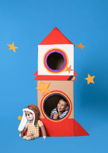 istock Cute little boy playing with cardboard rocket on light blue background 1398515652
