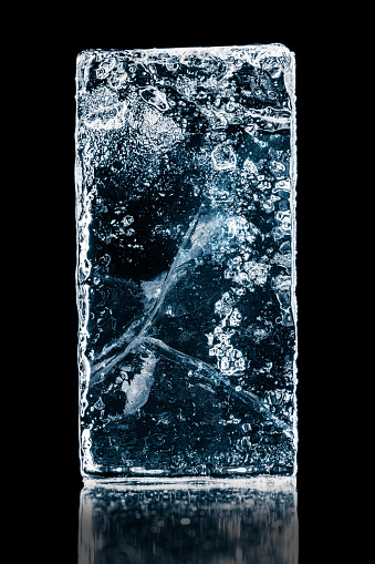 Crystal clear frosty textured natural ice block with cracks on black mirroring surface.