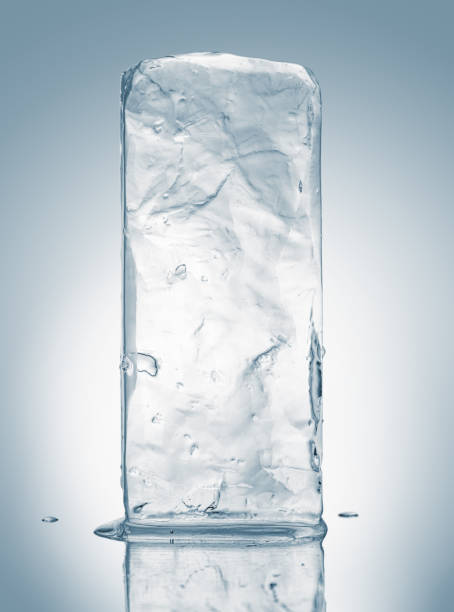 bloque de hielo natural cristalino en tonos azul claro sobre una superficie reflectante blanca. - blue transparent cold cube fotografías e imágenes de stock