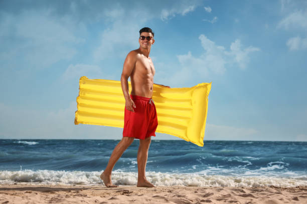 Man with yellow inflatable mattress at beach