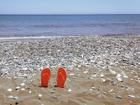 View of empty sea beach with pair of orange flip-flops in the sand