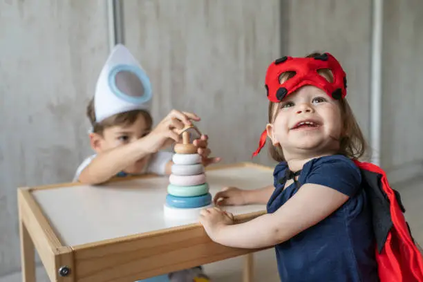Photo of Preschool boy and toddler girl brother and sister wearing costumes ladybug and rocket playing together at home children having fun growing up childhood and family concept copy space