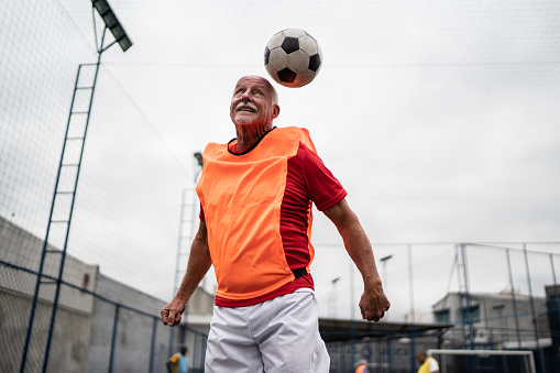 Senior man jumping to hit the ball with his head on the soccer field