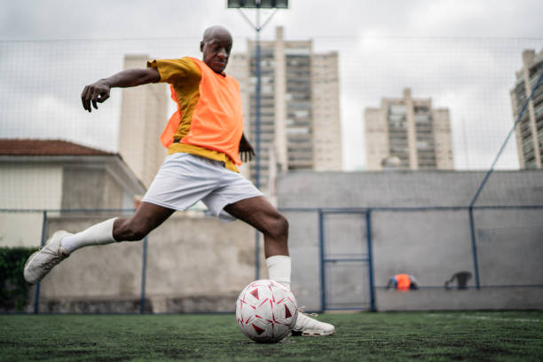 homme d’âge mûr donnant un coup de pied dans le ballon de football sur le terrain de football - penalty shot photos et images de collection