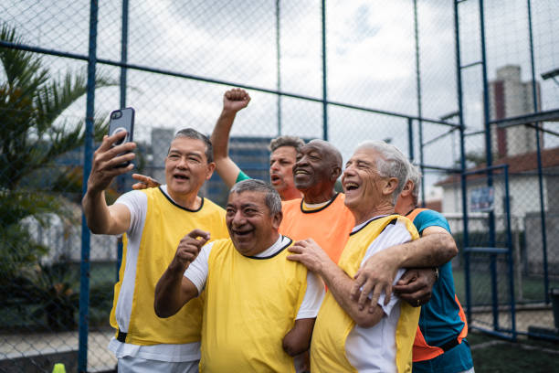Senior men taking selfies or filming using mobile phone on the soccer field