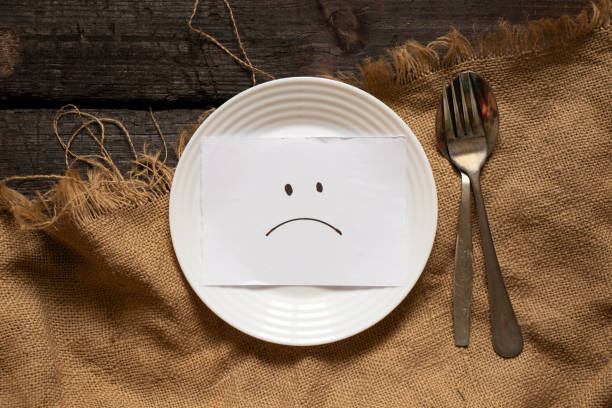 a sad smiley is drawn on paper lies on a white plate, on a wooden table and on a brown tablecloth, sadness and depression, crisis stock photo