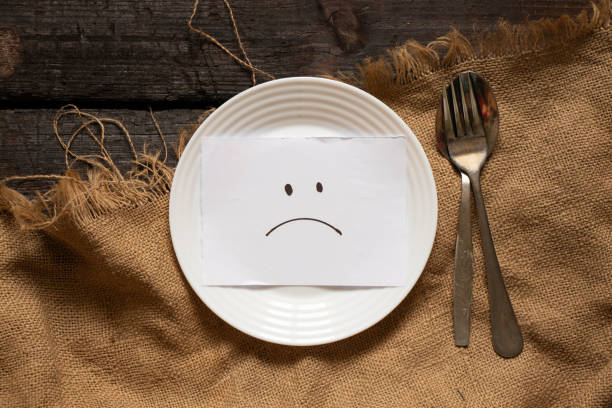 um sorriso triste é desenhado no papel está em um prato branco, em uma mesa de madeira e em uma toalha de mesa marrom, tristeza e depressão, crise - prato vazio - fotografias e filmes do acervo