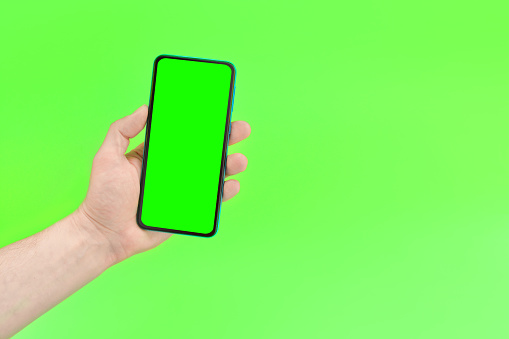 A man holds a smartphone with a green screen on green background.Mockup. Copy space for text