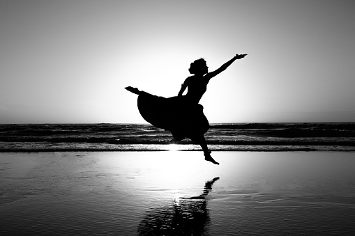 Woman in dress dancing/jumping on the beach at sunset, black and white photo