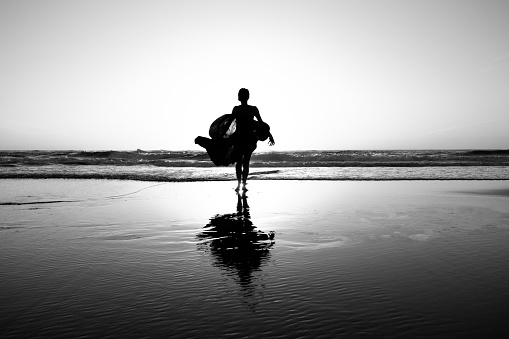 Woman in dress dancing/jumping on the beach at sunset, black and white photo