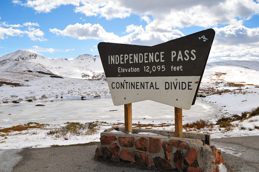 The sign at the top of Independence Pass and a frozen lake surrounded by early autumn snowfall on the mountains, Colorado, USA