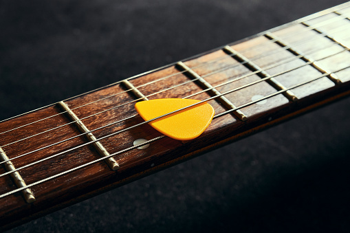 Yellow pick between the strings of an electric guitar close up