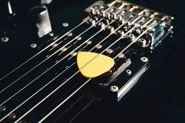 Pick between the strings on the soundboard of a black electric guitar close-up