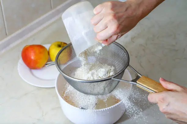 Sifting flour in dough. Cooking Charlotte apple pie