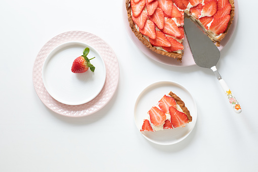 Delicious tart with custard cream and strawberries on a white table. Plates and spatula for dough application. Piece of grated on a plate. View from above.