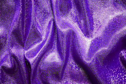 Shiny pleated fabric purple color top view and defocus