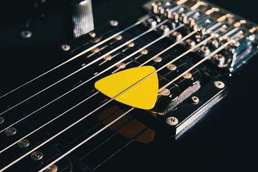 Yellow triangular plectrum between electric guitar strings