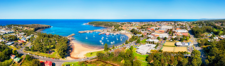 Sapphire coast town Ulladulla with scenic fishing marina and harbour behind breakwall on Pacific shores in Australia - aerial townscape panorama.