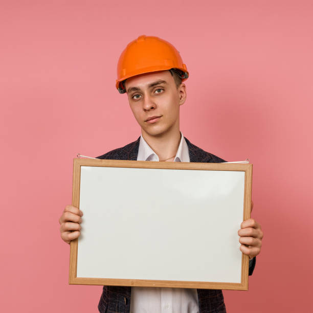 istock young engineer in a protective helmet and jacket with a white board in his hands on a pink background 1398551406