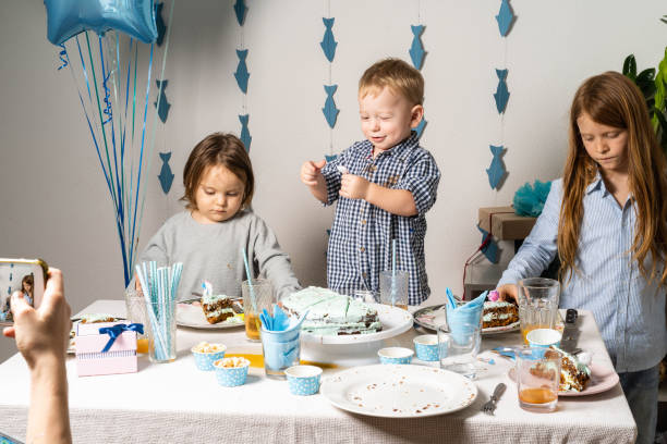 Brothers. Boy's birthday at the table. The boys at the table are cutting a birthday cake. Mom takes pictures of her child's birthday on the phone.