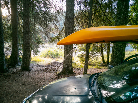 Driving SUV with yellow kayak on top to a mountain lake.