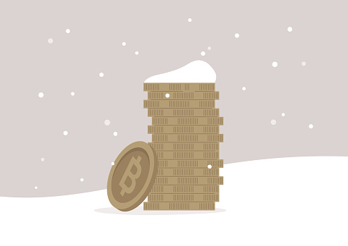 A crypto winter concept, a stack of bitcoins frozen into the ground and covered with snow