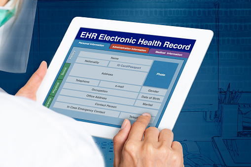 Picture looking through the shoulder of female doctor working on electronic health record by digital tablet.