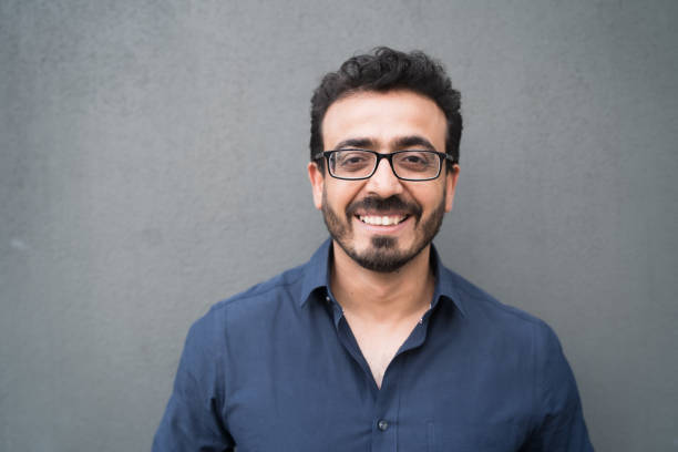 Man with toothy smile looking to camera. The shot of a happy man with smile on his face ,wearing eyeglasses looking to camera with gray background. pakistani ethnicity stock pictures, royalty-free photos & images